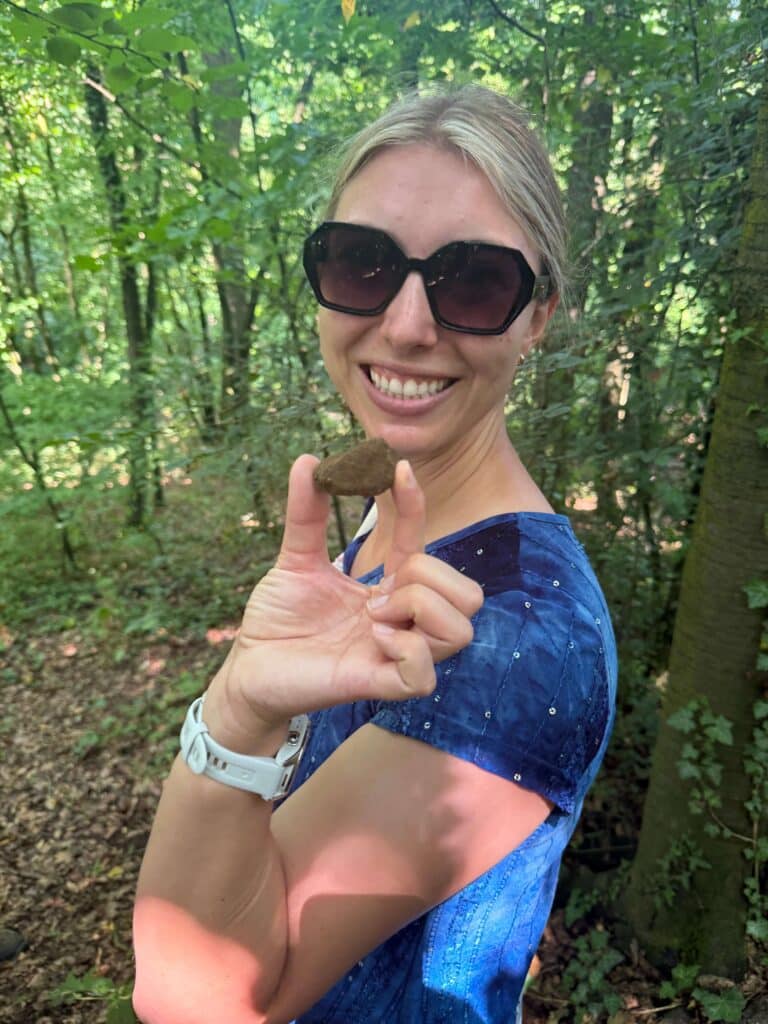 Woman wearing sunglasses holding a freshly dug truffle in her hand, with forest in the background.