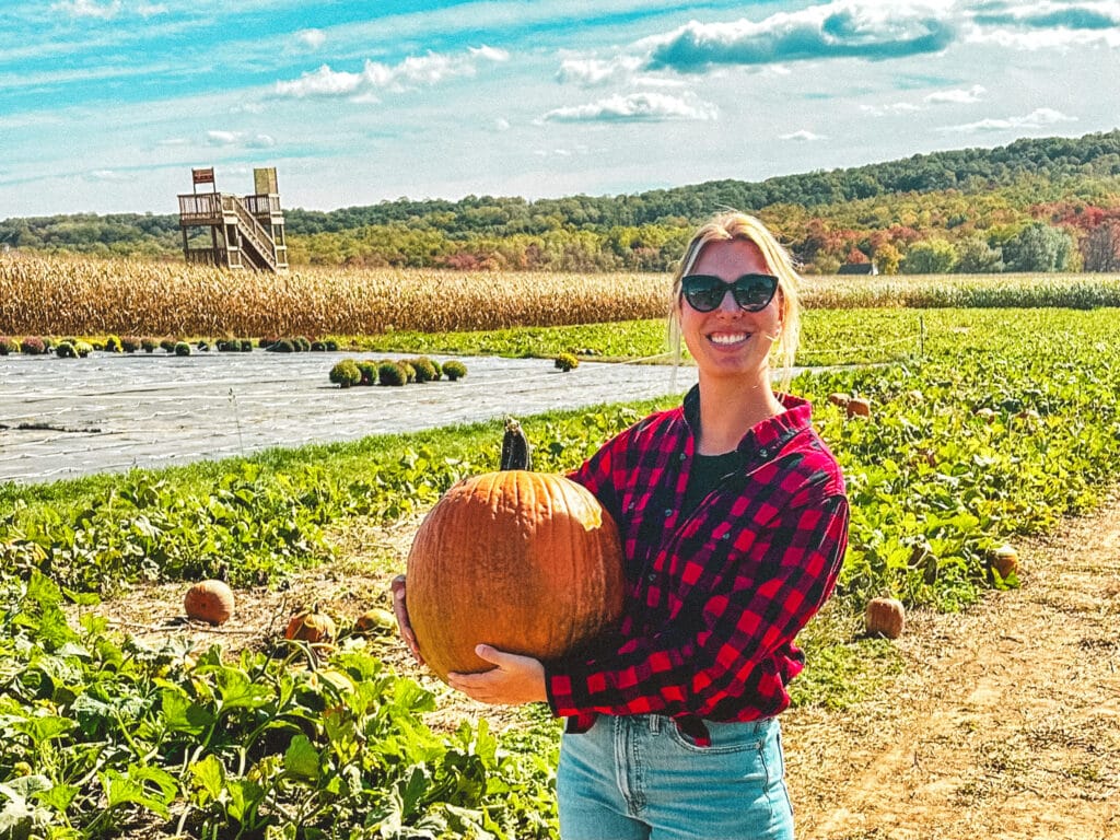 Person in plaid shirt holding a pumpkin in a Lancaster County field.