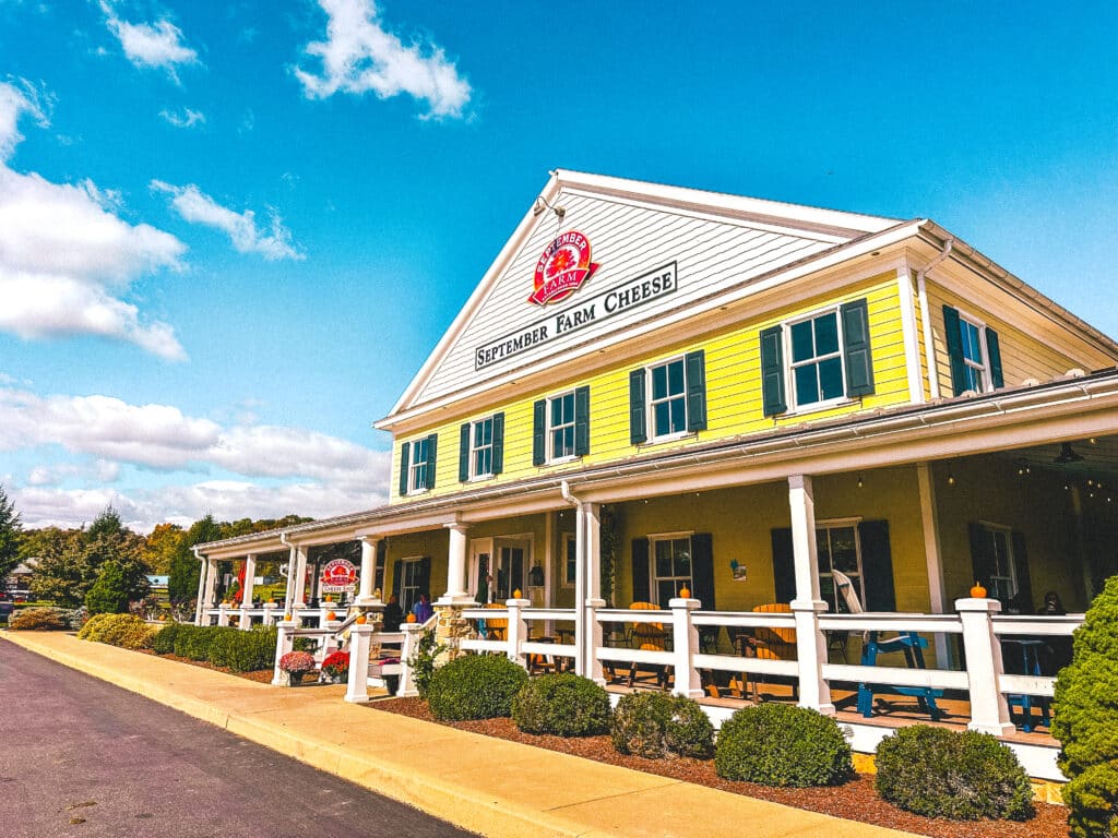 Exterior of September Farm Cheese shop with a yellow facade and white fence.
