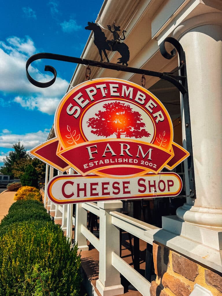 Hanging sign for September Farm Cheese mounted on a rustic wooden beam.