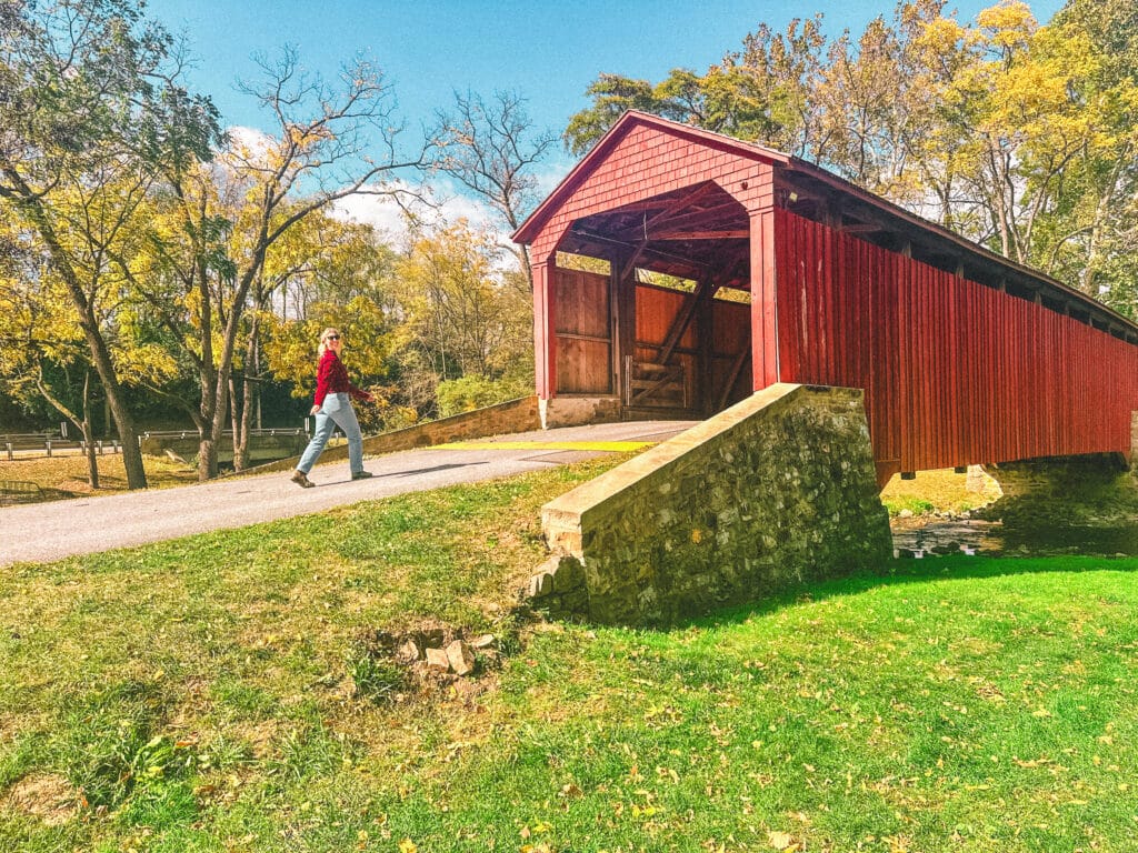 Red covered bridge with a person walking past on a sunny fall day.