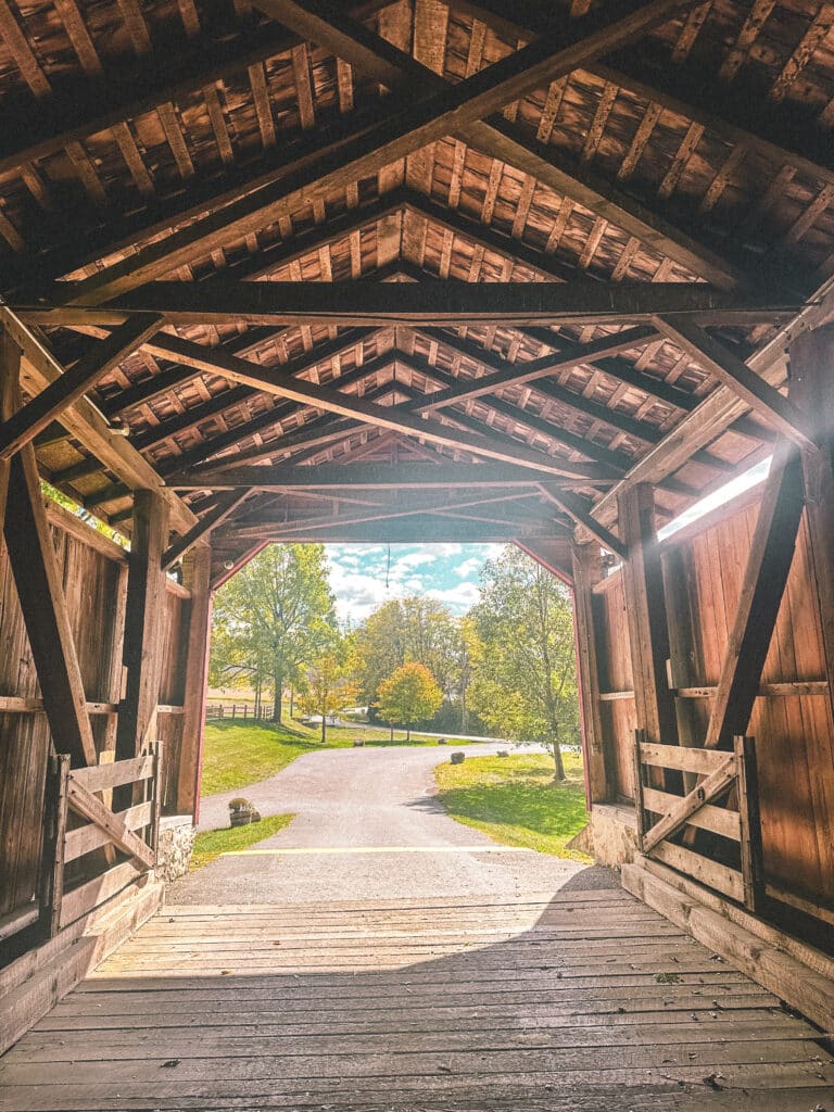 Inside view of a red covered bridge with wooden beams and open views on both ends.