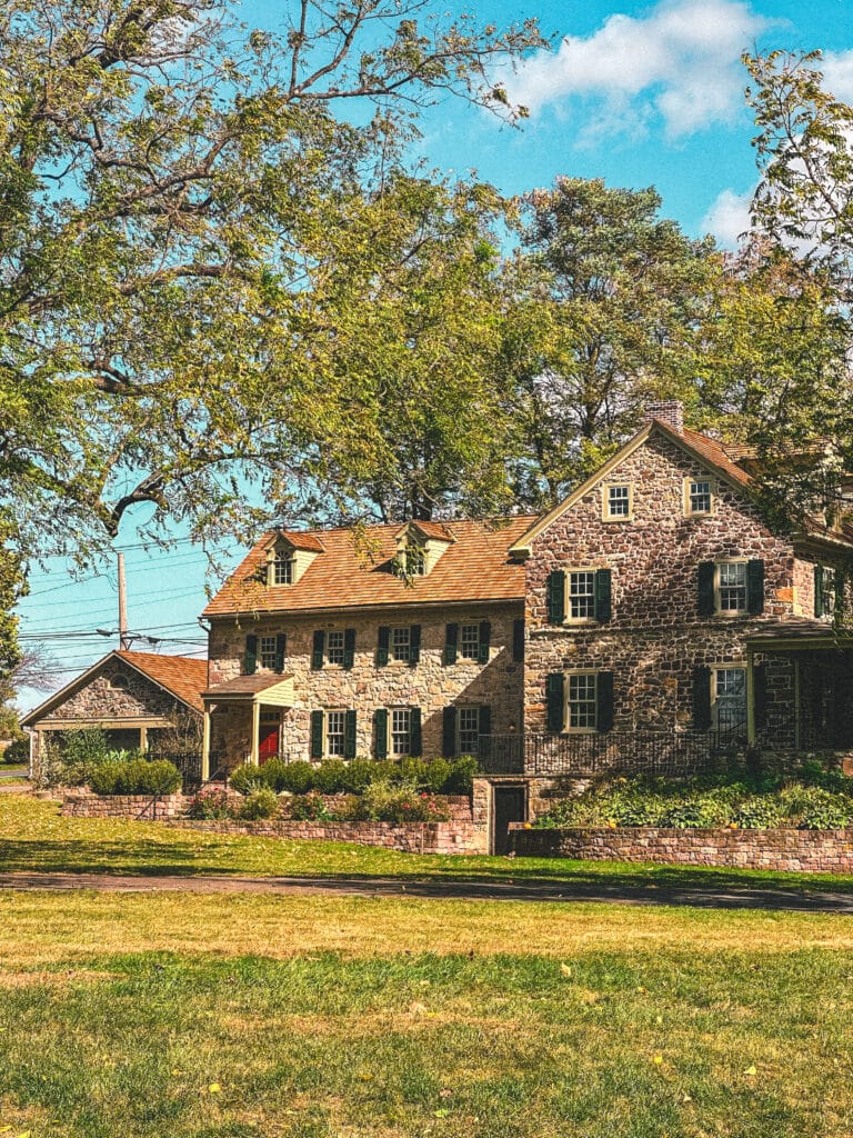 Historic stone house surrounded by trees with light fall color.