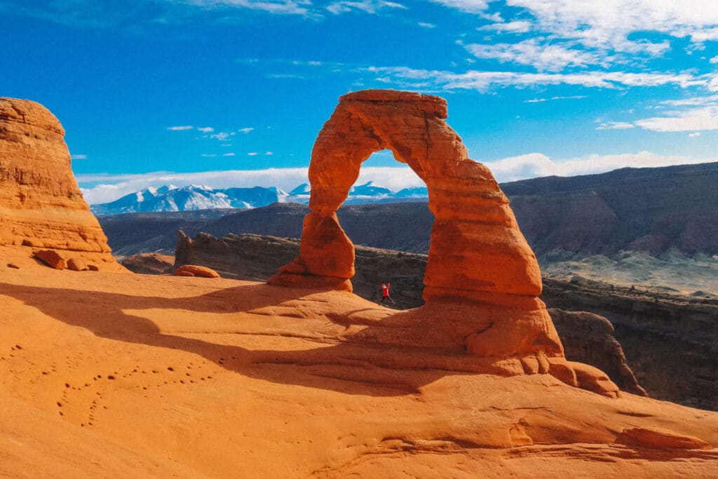 Delicate Arch glowing orange under a crisp bright blue sky in winter, with snowy La Sal mountains in the background