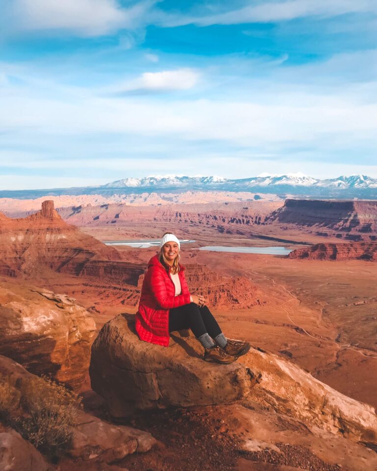Adventurer in a red parka and a white beanie posing at Deadhorse point