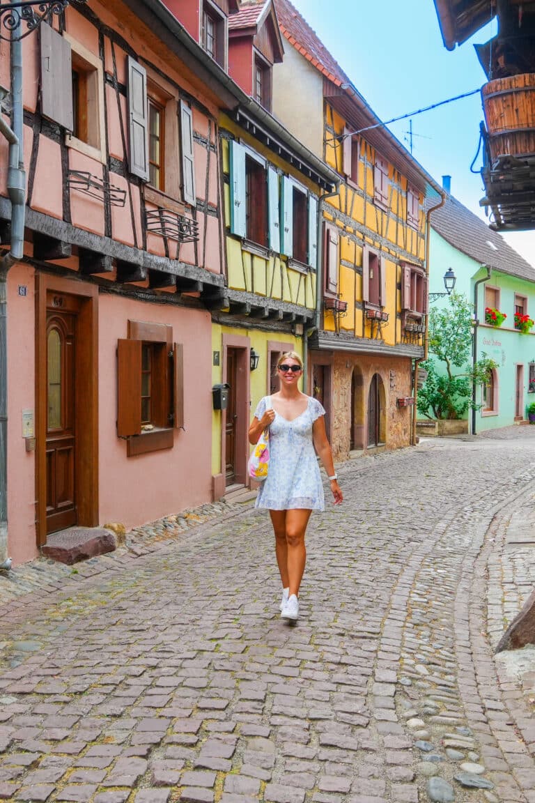 Woman in a white dress walking down a colorful street in Eguisheim.