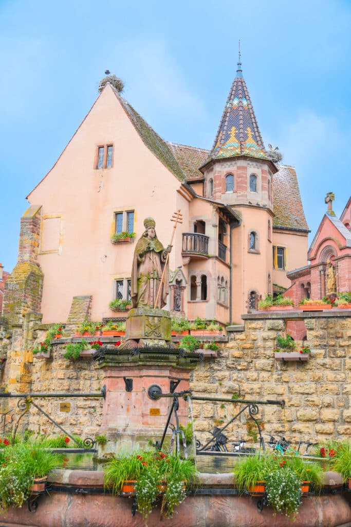 Exterior of Eguisheim’s pink church with castle-like spire and stone terrace.