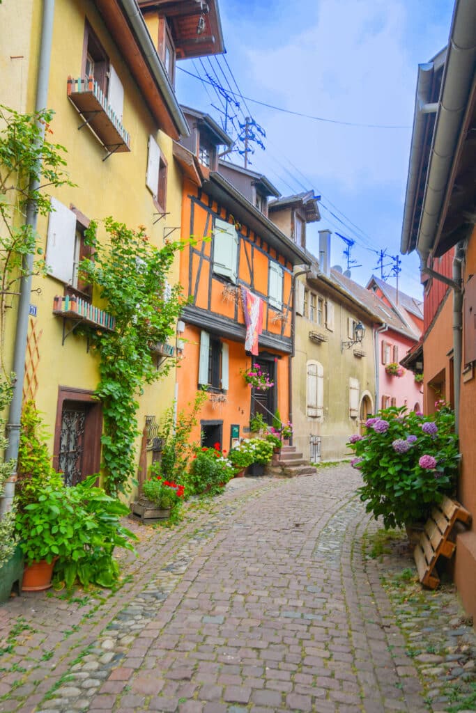Narrow alley in Eguisheim framed by colorful shuttered houses and cobblestone path.