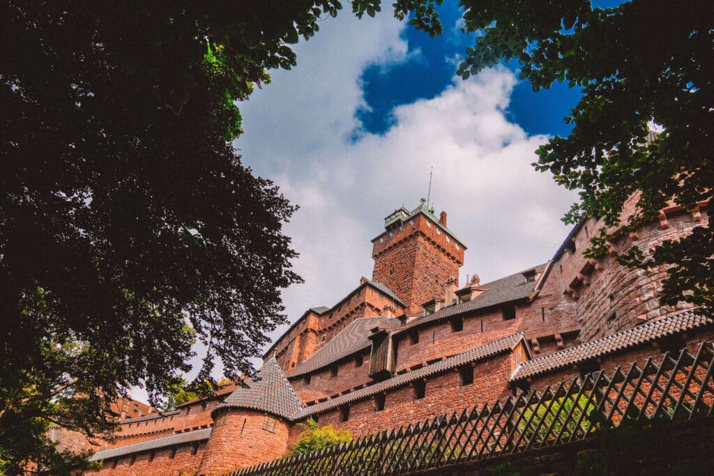 Exterior of Château du Haut-Koenigsbourg, framed by trees with a dramatic sky above.