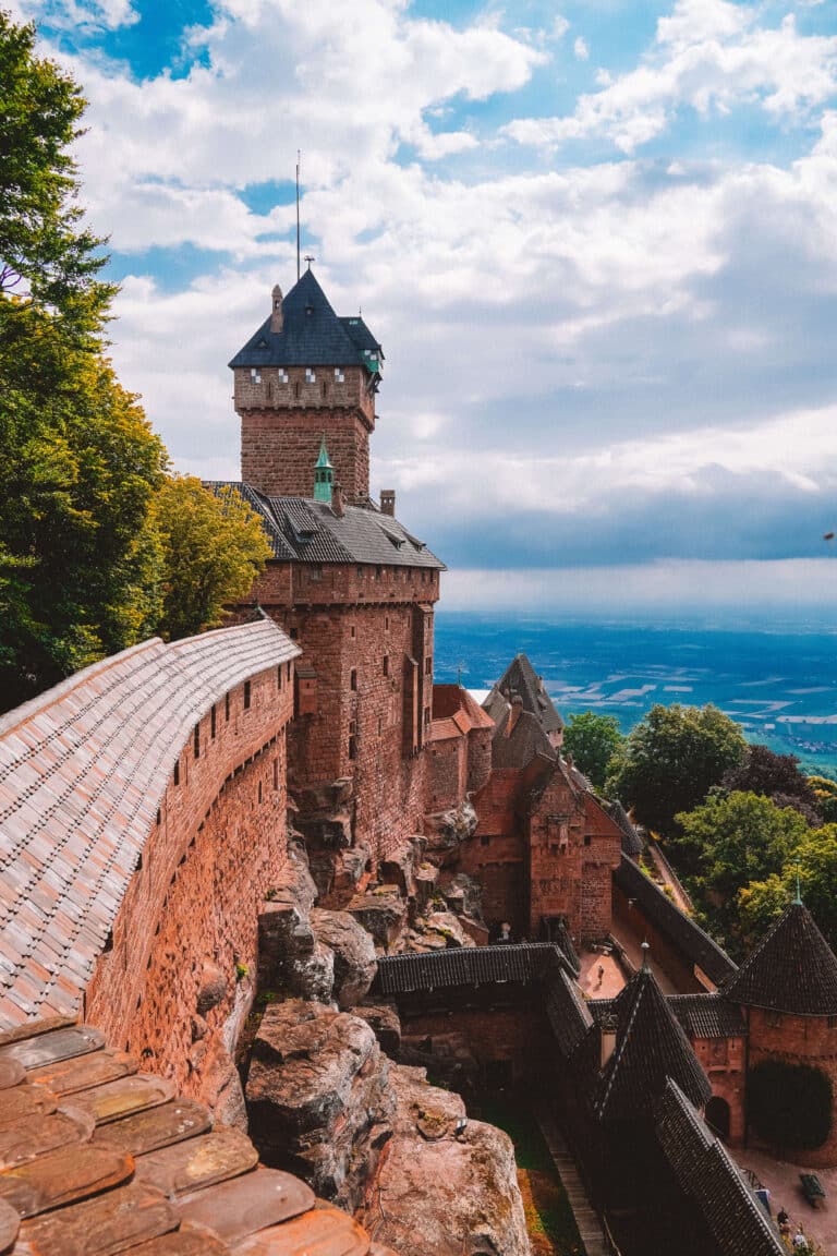 View of Château du Haut-Koenigsbourg’s stone ramparts and tower overlooking the Alsace plain under a partly cloudy sky.
