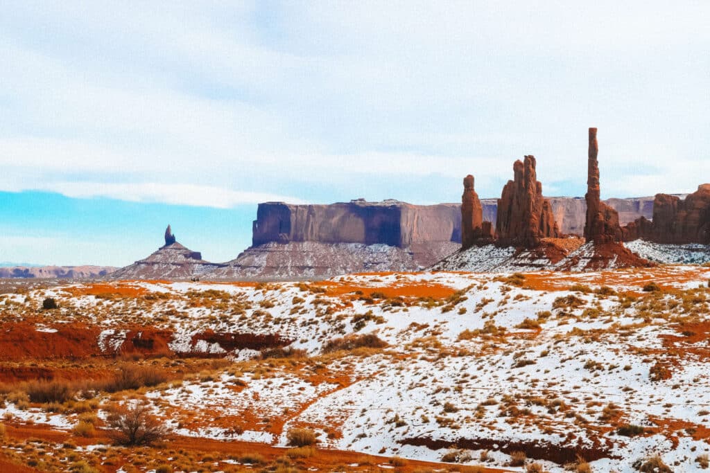 Monument Valley formations rising beyond a snowy desert field under a crisp blue sky.
