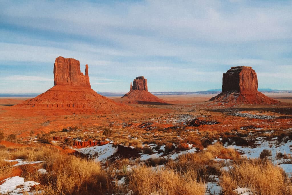 Wide view of East and West Mittens at Monument Valley glowing in golden afternoon light with tufts of dry grass.