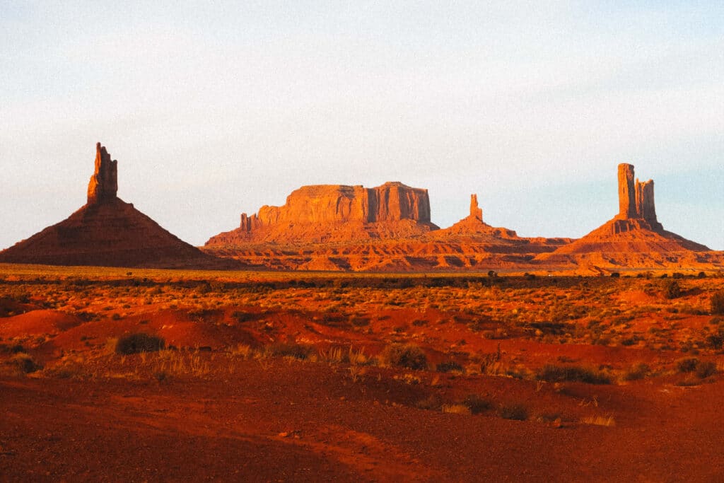 Monument Valley formations rising beyond a snowy desert field under a crisp blue sky.