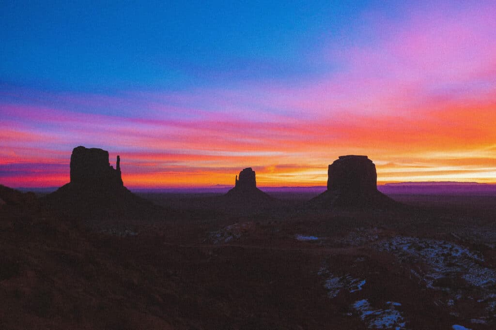 Sunrise silhouette of the Mittens and Merrick Butte, glowing in purples, pinks, and blues as seen from The View Hotel