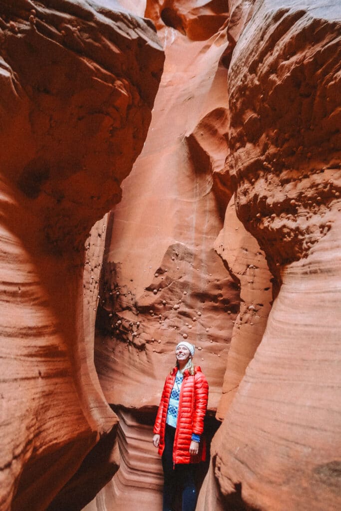 Hiker in a red jacket walking through the entrance of Wind Pebble Canyon, surrounded by smooth, towering sandstone walls