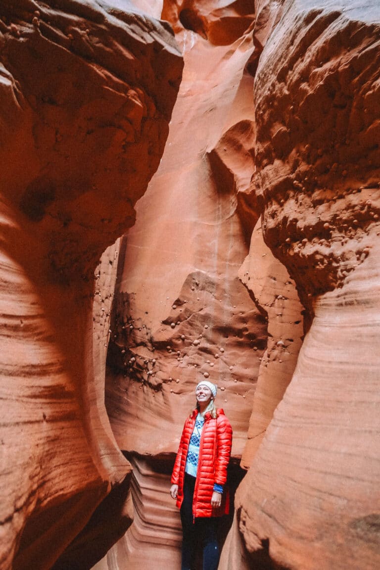 Hiker in a red jacket walking through the entrance of Wind Pebble Canyon, surrounded by smooth, towering sandstone walls