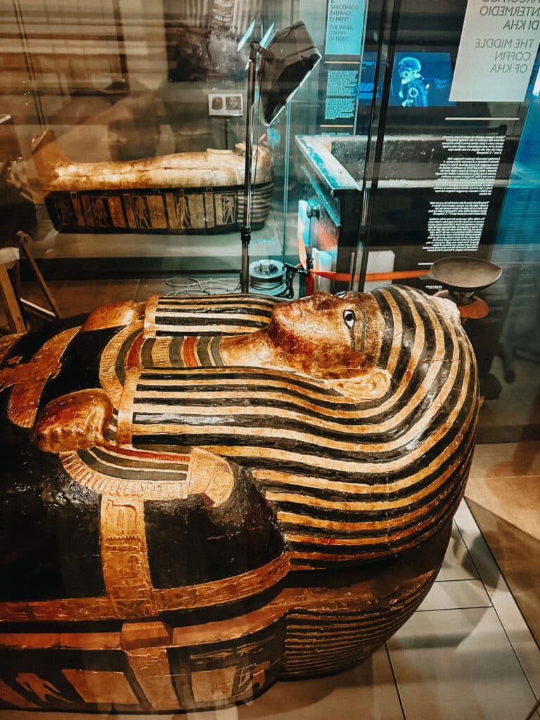 Close-up of a richly painted sarcophagus lid with gold and black stripes on display at the Museo Egizio in Turin.