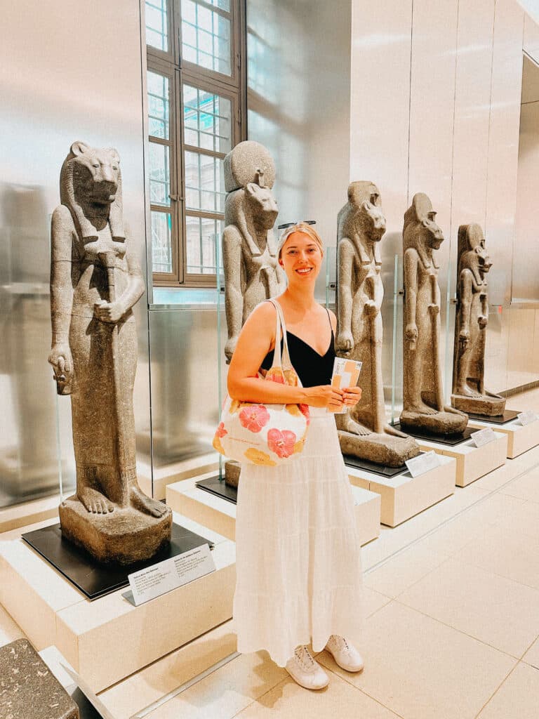 Visitor standing among a row of ancient statues in a well-lit gallery room at the Egyptian Museum in Turin.
