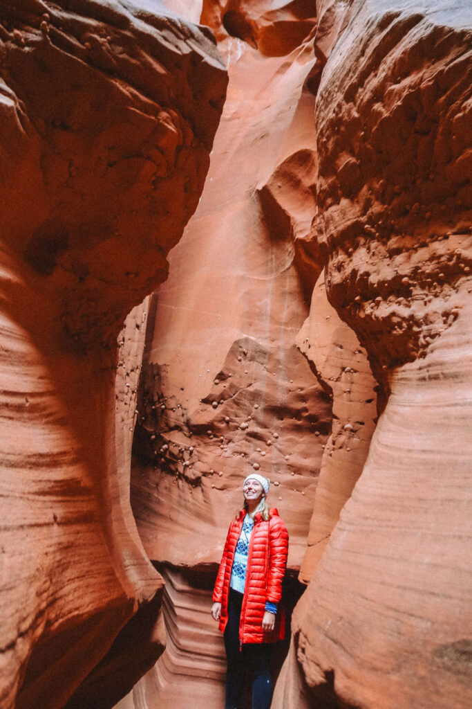 Hiker in a red jacket walking through the entrance of Wind Pebble Canyon, surrounded by smooth, towering sandstone walls