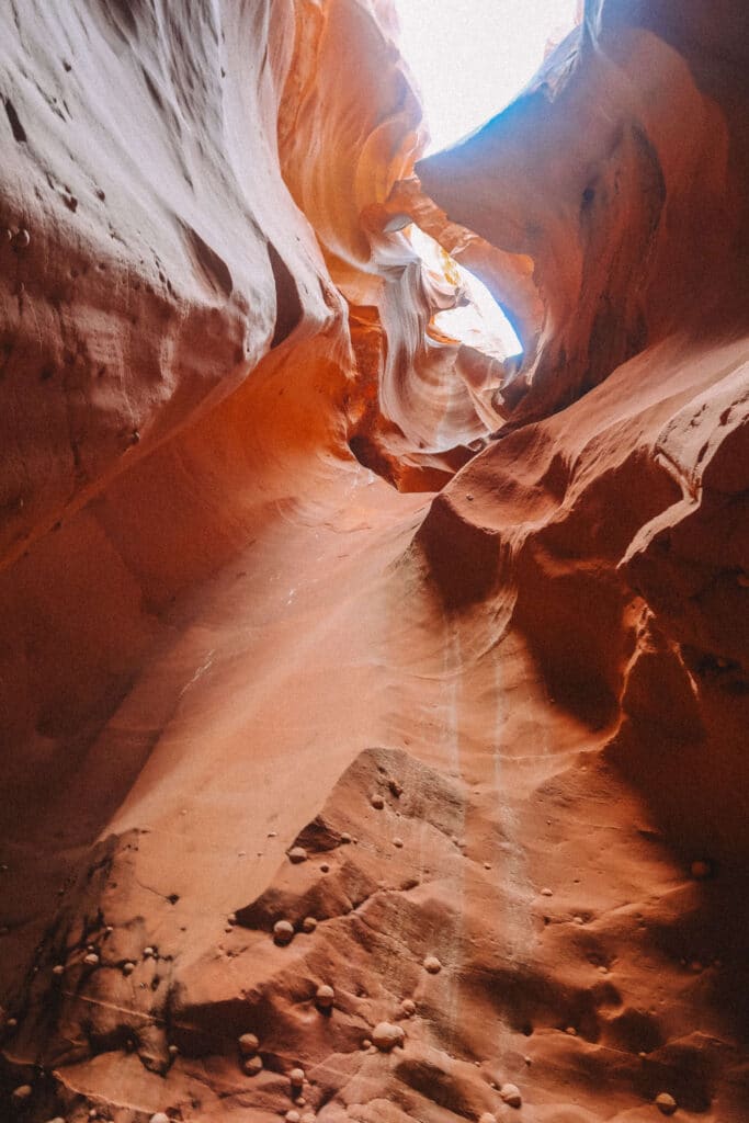 Softly lit slot canyon interior in Wind Pebble Canyon, with curving red rock formations and a patch of light from above