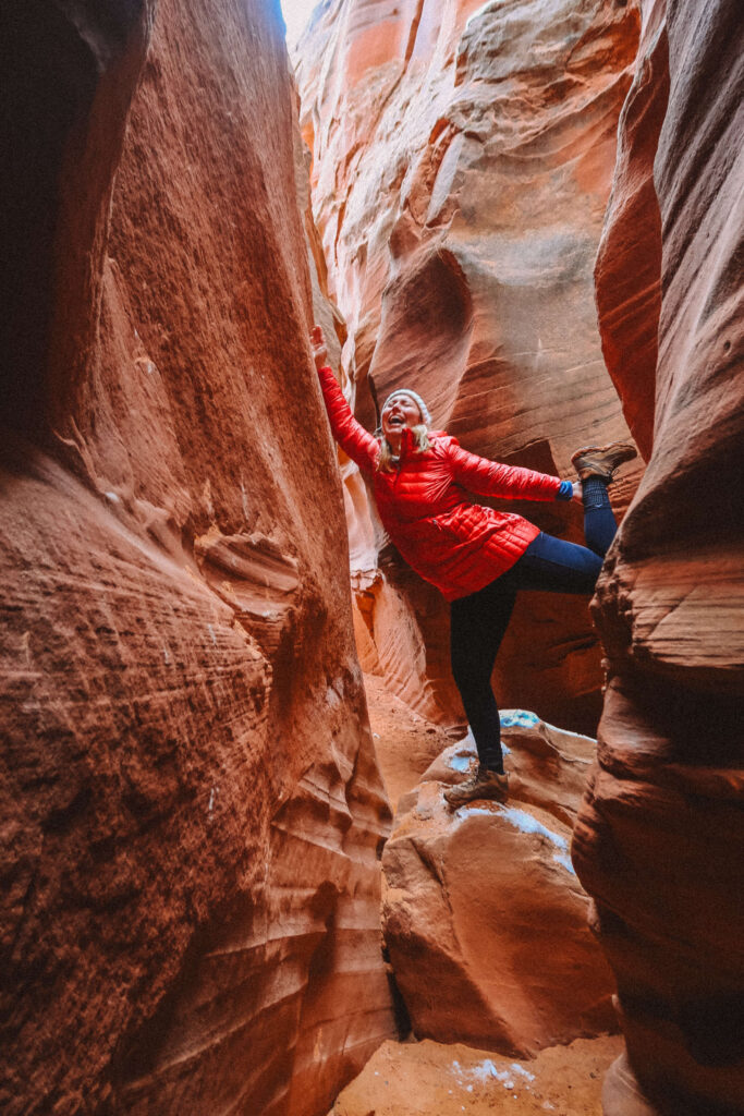 Hiker climbing carefully through a narrow sandstone corridor inside Wind Pebble Canyon, showcasing the textured canyon walls