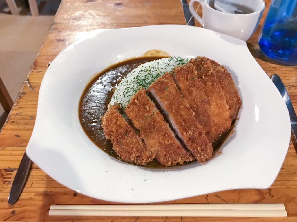 Plate of Japanese katsu curry with a sliced breaded cutlet served on white ceramic dish with chopsticks on the side.