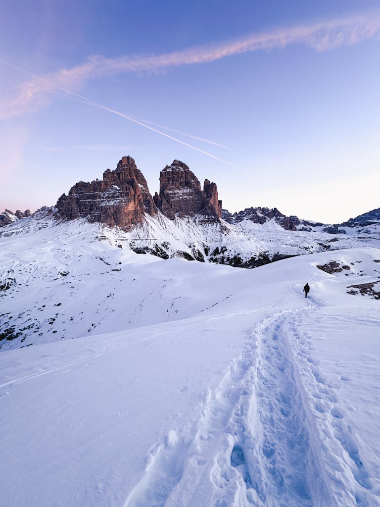 A tranquil scene of Tre Cime di Lavaredo during winter at sunrise, showcasing snowy trails.