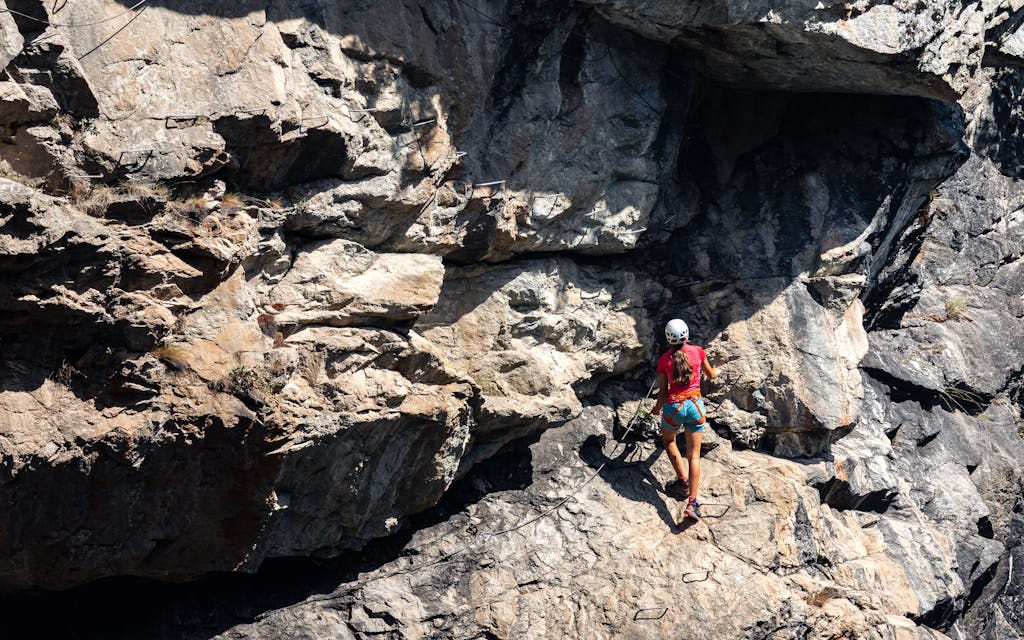 A woman skillfully climbs a rugged cliff face on a sunny summer day.