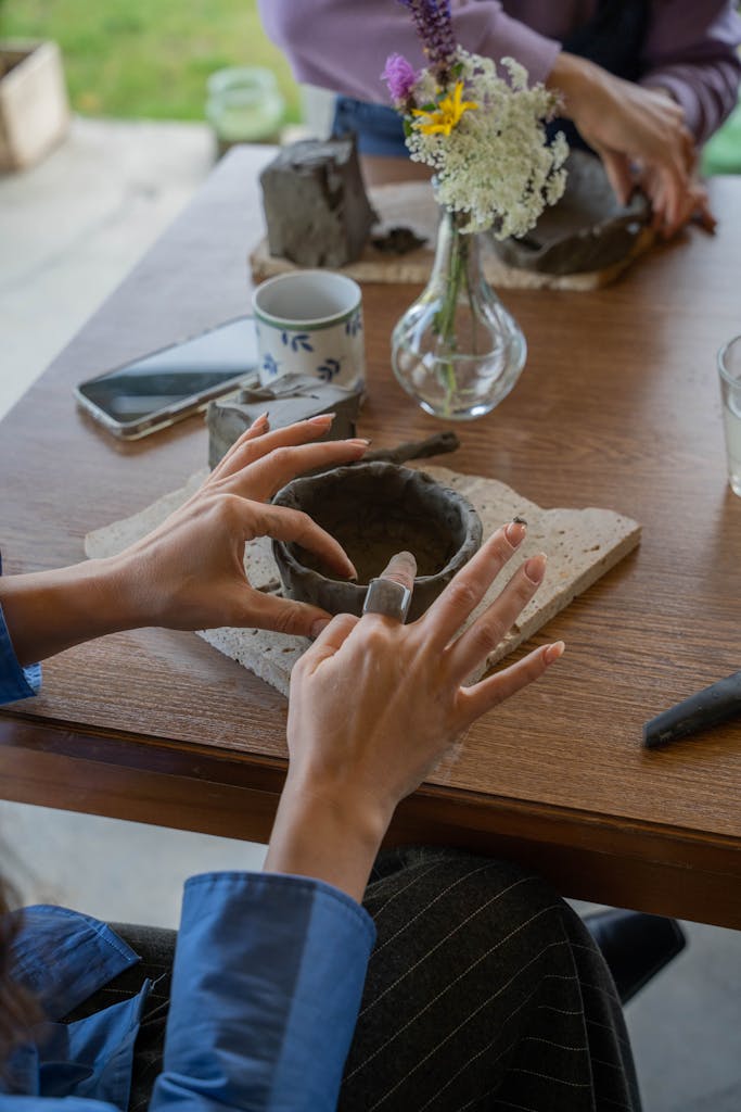 Close-up of adult hands shaping clay on table during pottery class, various tools visible.