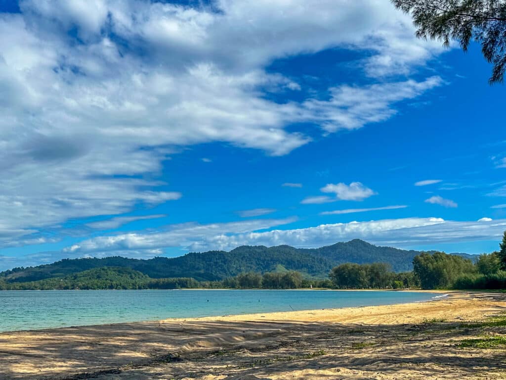 Scenic view of the Khao Lak coastline with blue skies, sea, and forested hills in the distance.