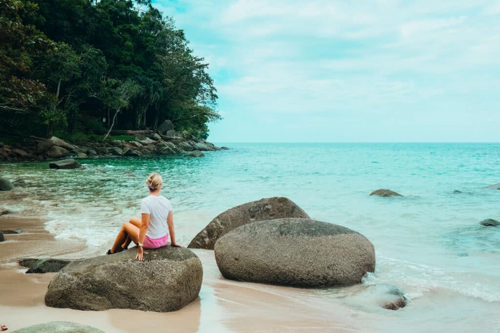 Traveler sitting on rocks at the Beach with turquoise waves and jungle backdrop in Khao Lak–Lam Ru National Park
