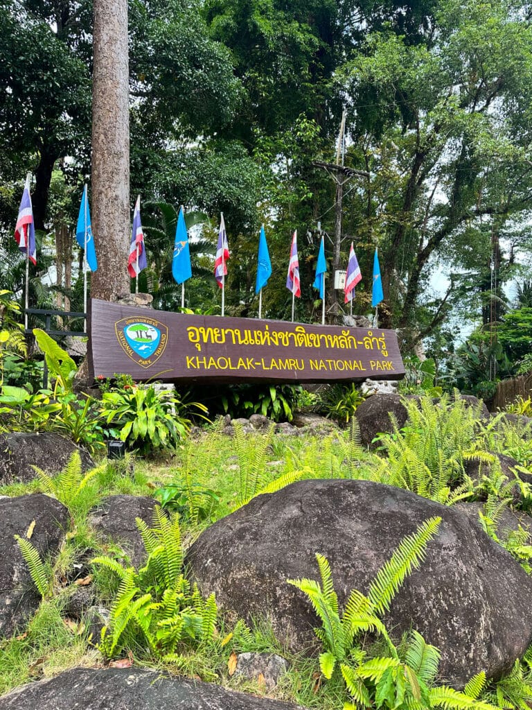 Entrance sign for Khao Lak–Lam Ru National Park surrounded by ferns, rocks, and tropical forest