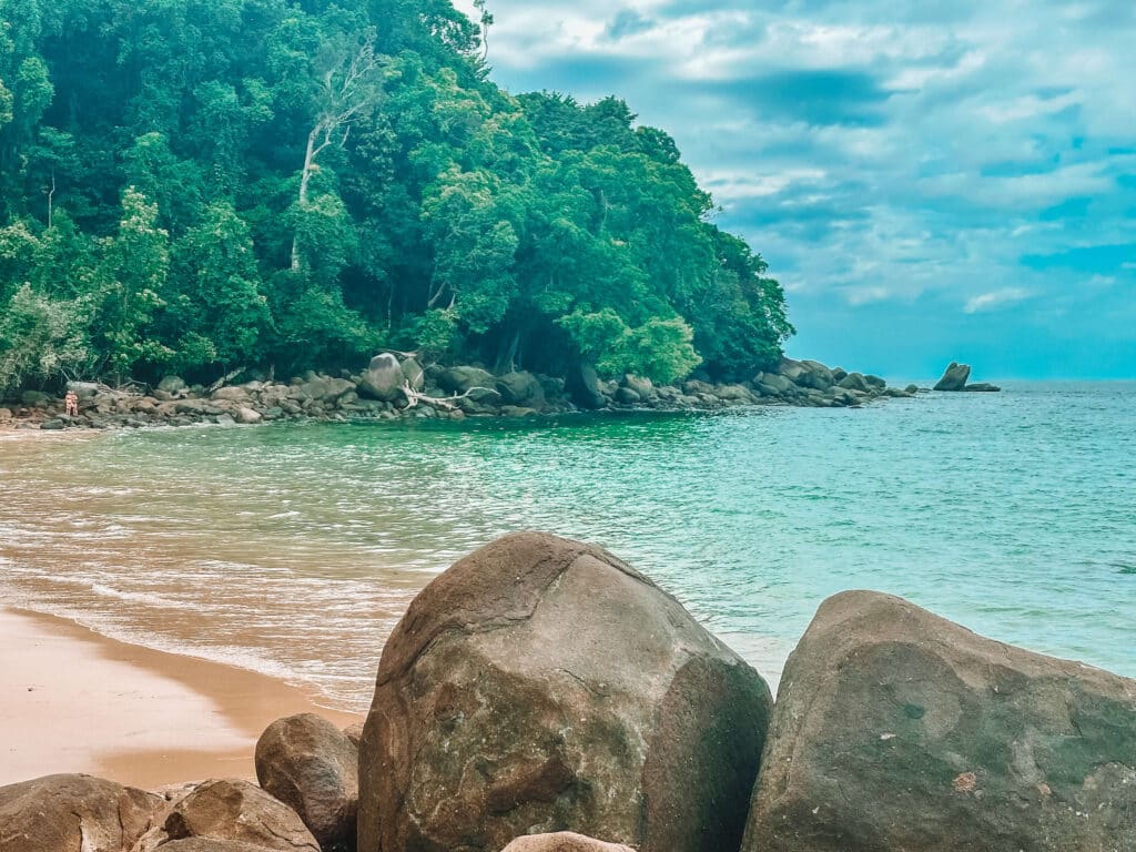 Small Sandy Beach framed by jungle and large rocks, with calm turquoise water in Khao Lak–Lam Ru National Park