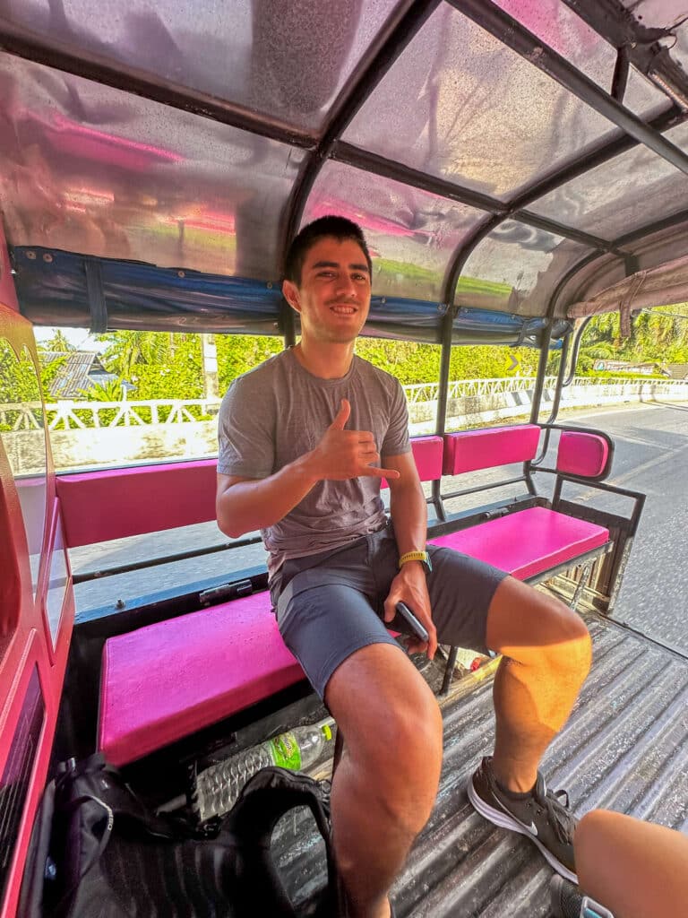 Rider sitting in the back of a pink open-air tuk-tuk taxi in Khao Lak, Thailand.