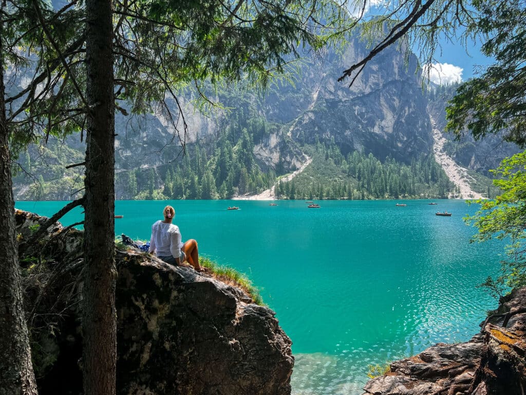 Traveler sitting on a lakeside rock at Lago di Braies, looking out over emerald water and forested cliffs