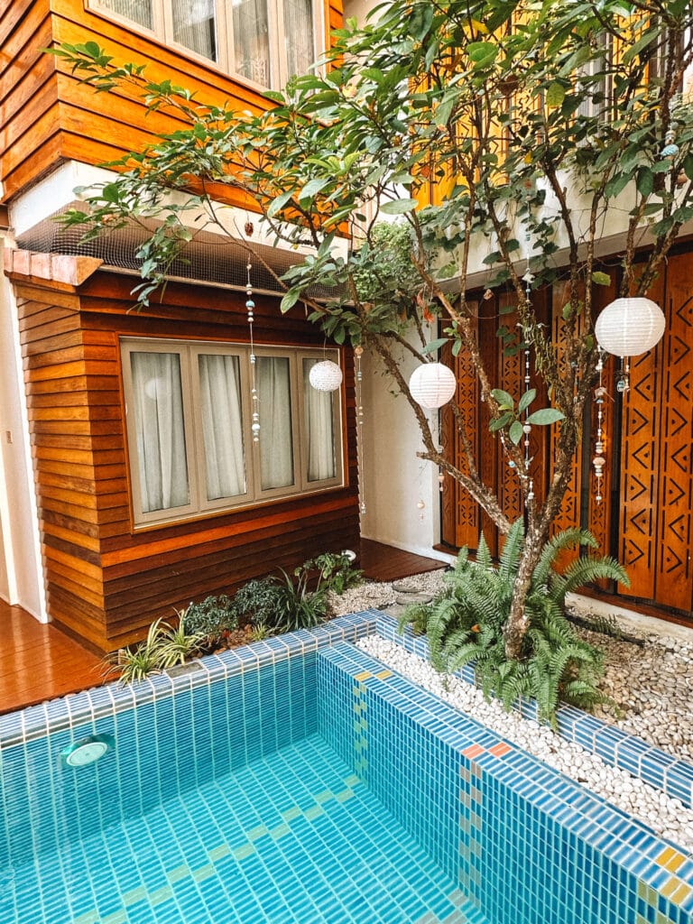 Leafy courtyard and saltwater pool surrounded by wooden architecture at Pastell Oldtown Chiang Mai.