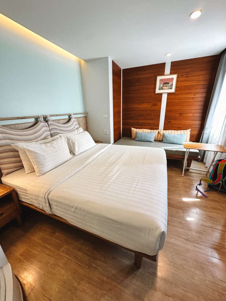 Modern guest room at Pastell Oldtown Chiang Mai featuring a king bed, desk, and wooden accent wall.