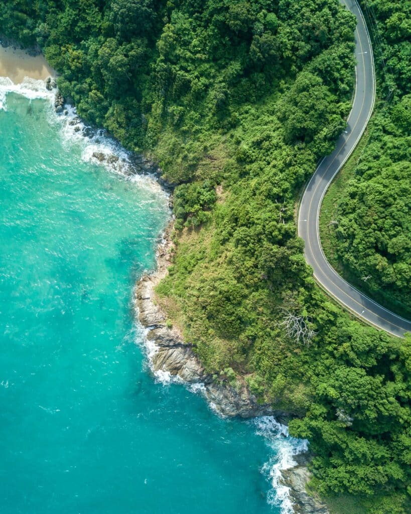 Aerial view of a winding coastal road hugging turquoise water and lush green cliffs in southern Thailand.
(Unsplash photographer credit: Scott Taylor)