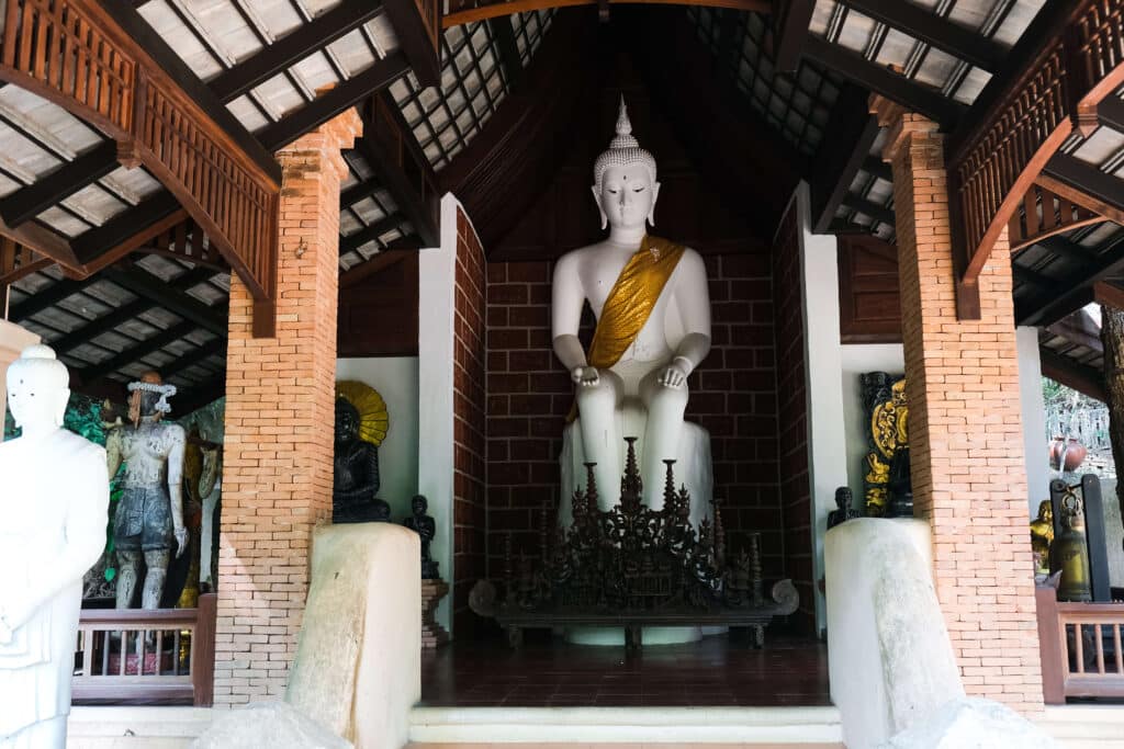 Indoor Buddha statue seated in a shrine with tall brick pillars at Wat Pha Lat.