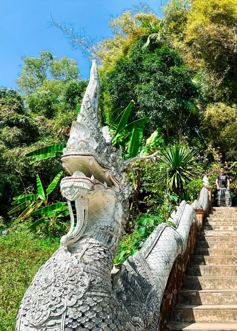 Ornate naga dragon statues lining the stairway to Wat Pha Lat temple, surrounded by jungle.