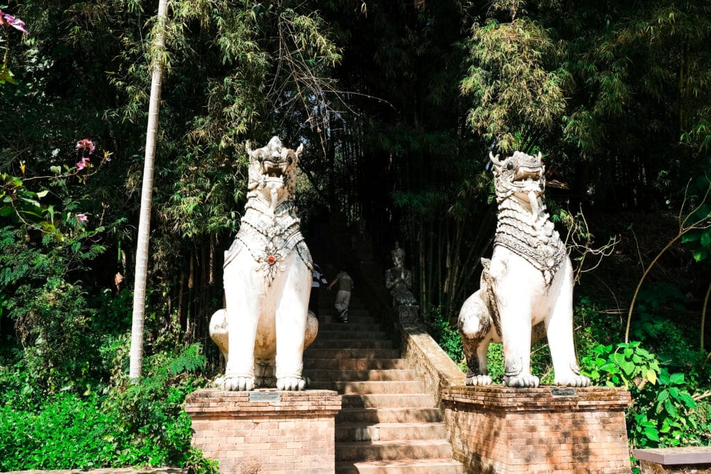 Stone lion statues flanking a staircase surrounded by forest at Wat Pha Lat in Chiang Mai.