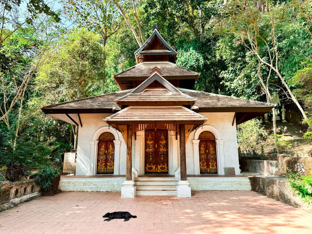 Front view of a small temple at Wat Pha Lat with a black dog laying in the foreground.
