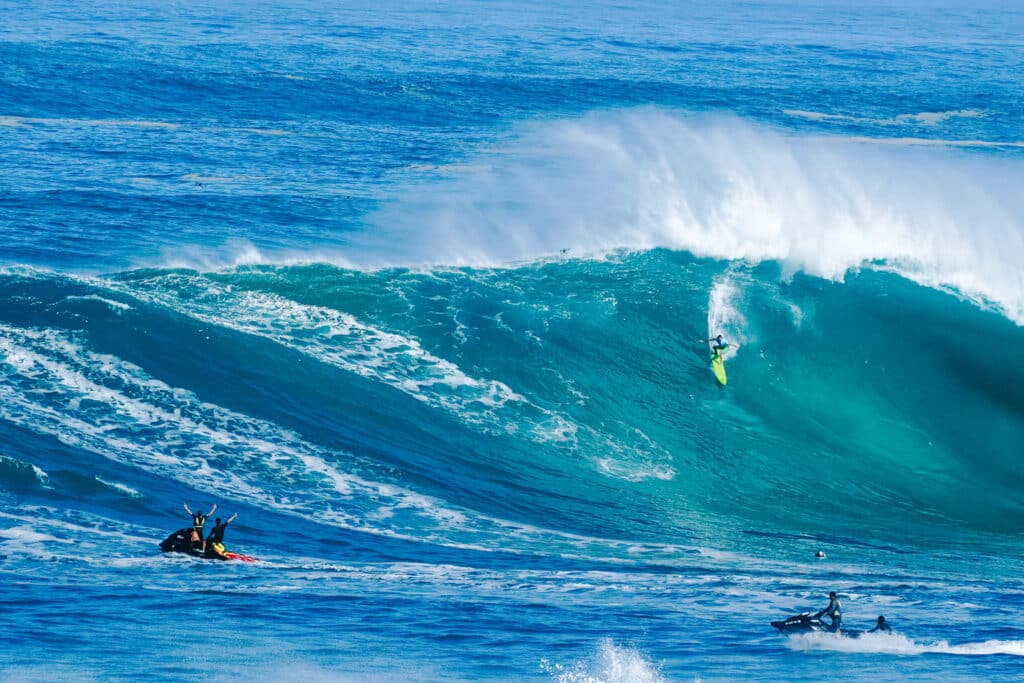 Tall peeling wave at Waimea Bay with a surfer dropping down the face.