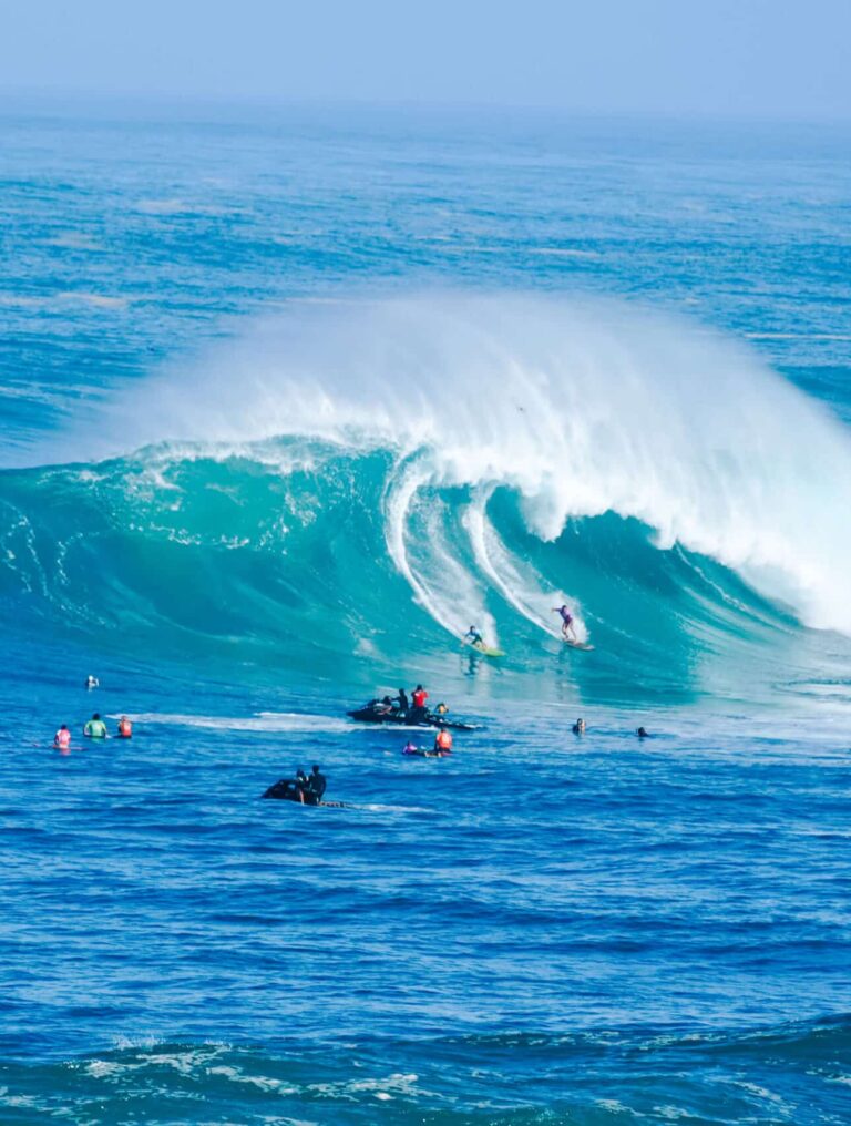A huge wave crashing with mist rising into a faint rainbow above the spray.