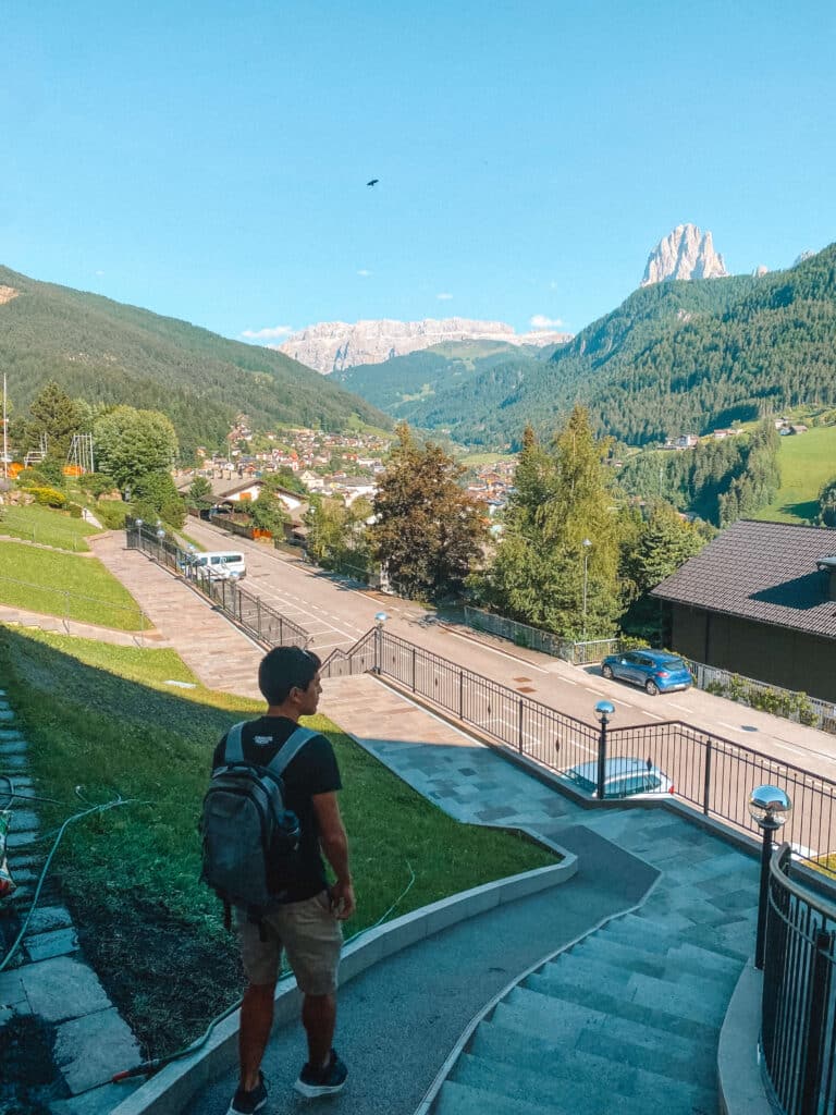 Traveler walking up the quiet residential street toward Bnb Lavi and the free parking with Dolomite peaks in the background.