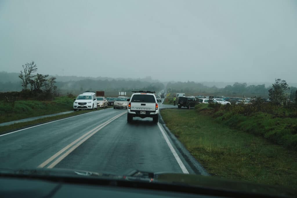 Cars driving through misty, overcast weather near Hawaiʻi Volcanoes National Park during an eruption event.
