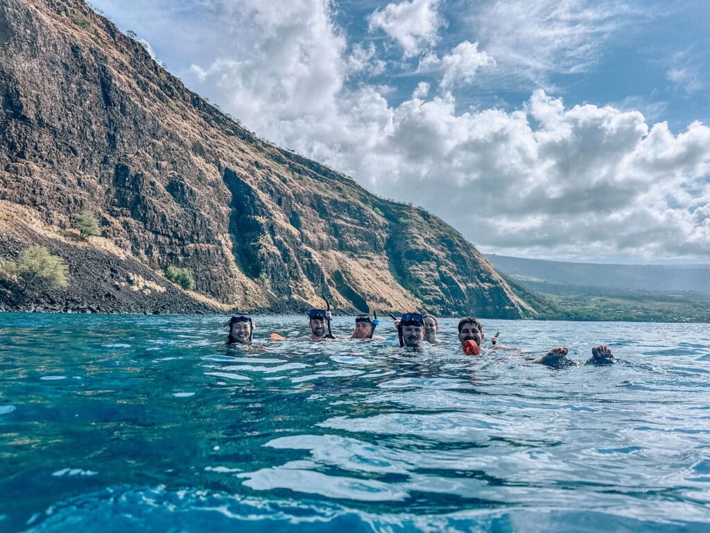 A small group of snorkelers swimming together toward the cliffs of Kealakekua Bay.