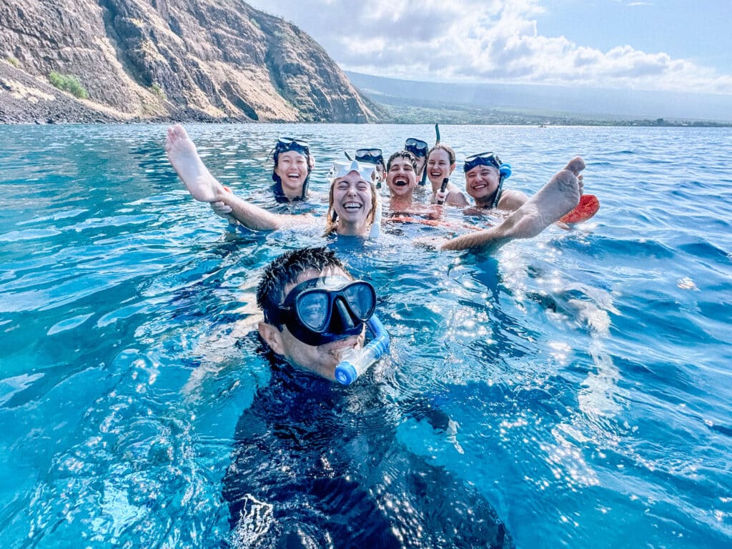 Snorkelers laughing and posing for a photo in the clear blue waters of Kealakekua Bay.
