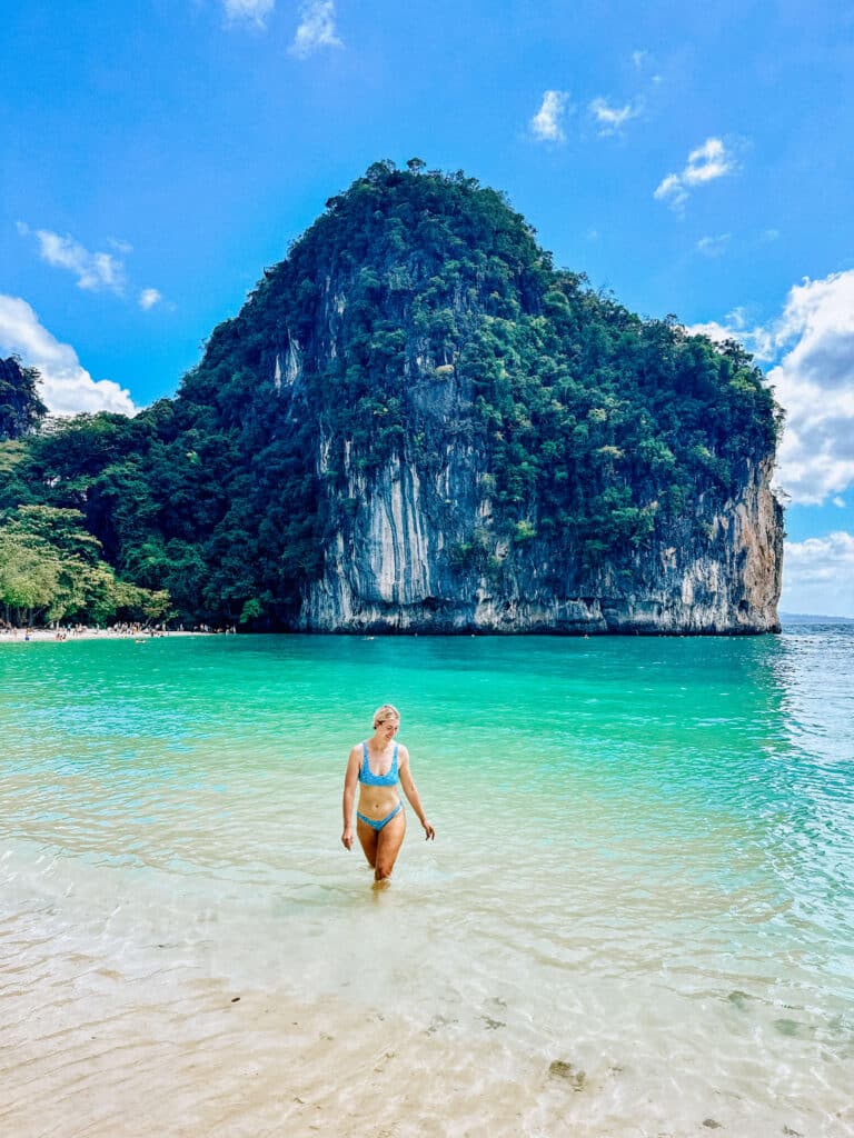 A traveler standing knee-deep in clear turquoise water with Hong Island’s dramatic limestone backdrop behind them.
