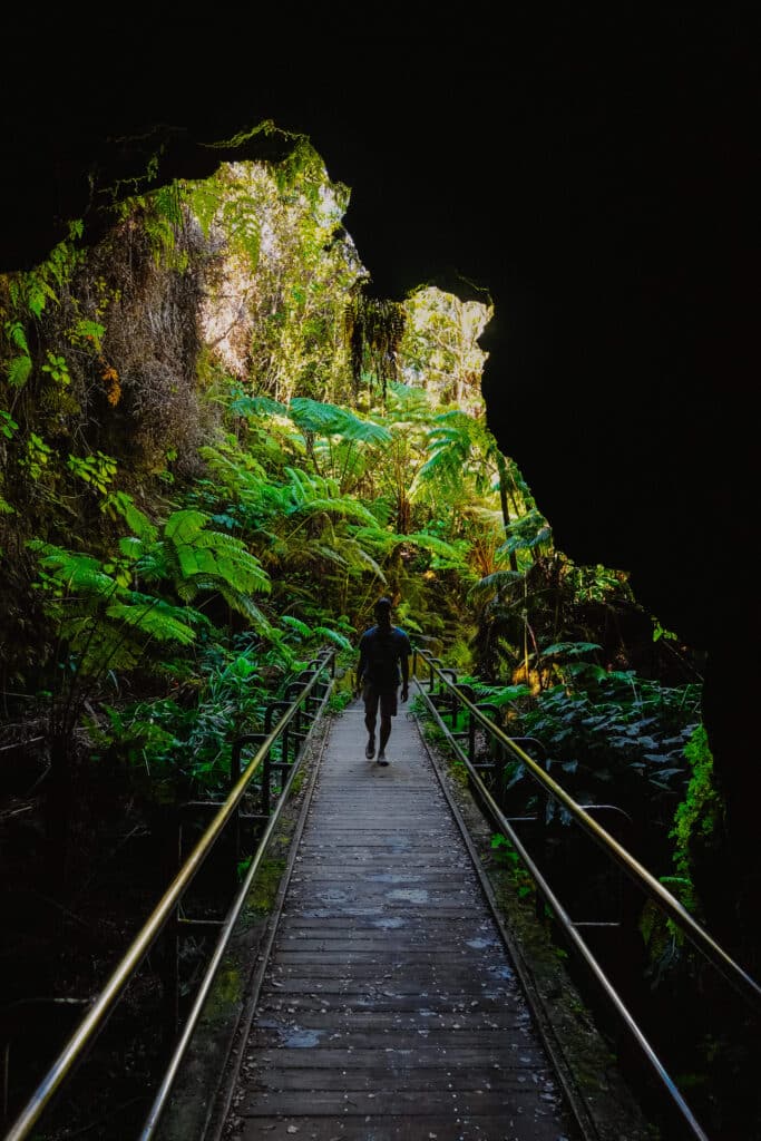 Inside the Nāʻhuku Lava Tube, showing the illuminated tunnel walls and a visitor walking along the pathway.